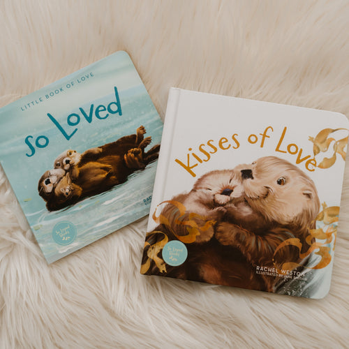 Two children's board books about sea otters, titled 'So Loved' and 'Kisses of Love', displayed on a soft white faux fur surface.
